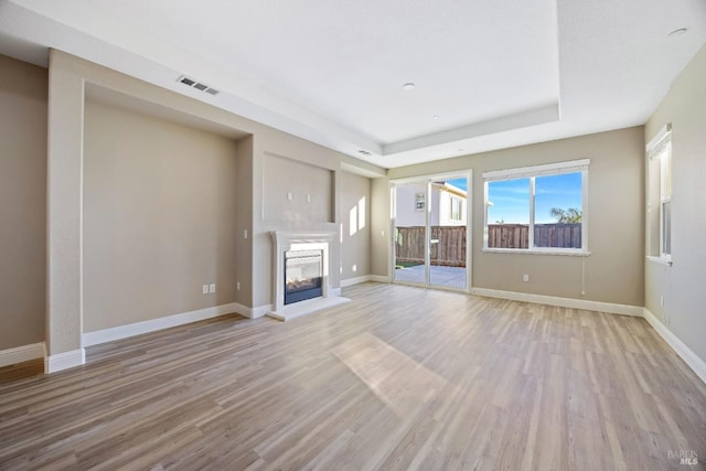 unfurnished living room with wood finished floors, visible vents, a multi sided fireplace, and a tray ceiling