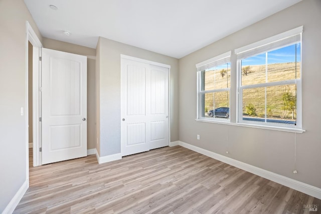 unfurnished bedroom with light wood-style flooring, baseboards, and multiple windows