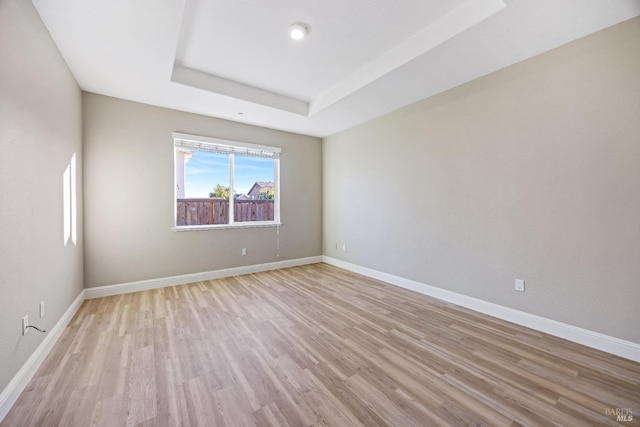 unfurnished room with light wood-style floors, baseboards, and a raised ceiling