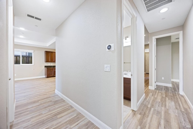 corridor featuring baseboards, visible vents, a textured wall, and light wood finished floors