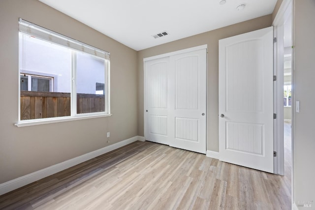 unfurnished bedroom with baseboards, wood finished floors, visible vents, and a closet