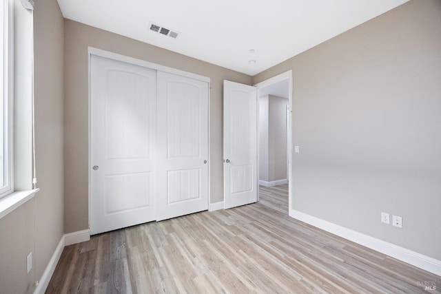 unfurnished bedroom with a closet, light wood-style floors, visible vents, and baseboards