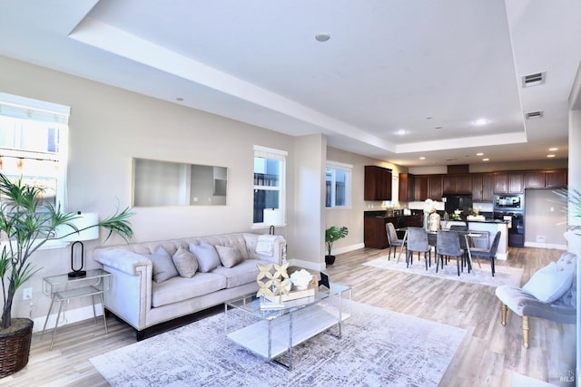 living room featuring light wood-style flooring, a tray ceiling, visible vents, baseboards, and recessed lighting