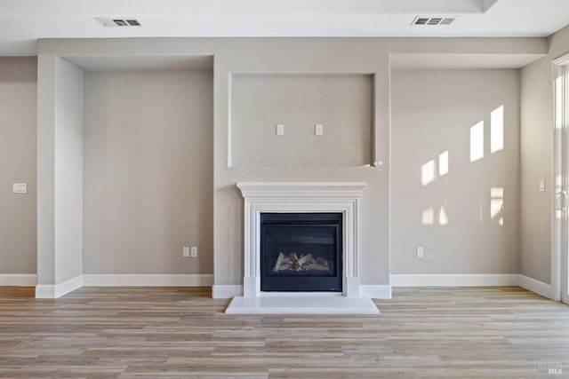 unfurnished living room with light wood-type flooring, baseboards, visible vents, and a glass covered fireplace