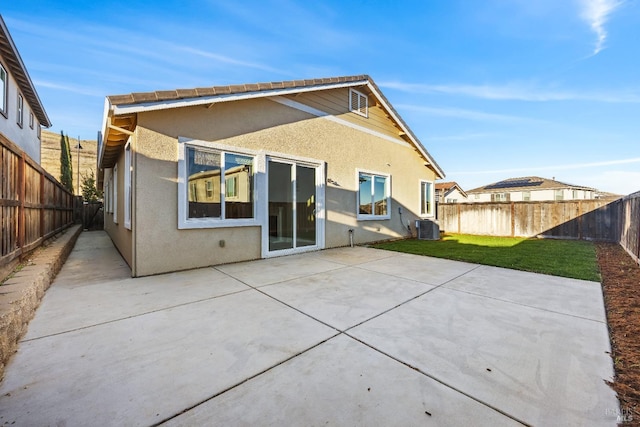 back of house featuring a fenced backyard, central AC unit, a yard, a patio, and stucco siding