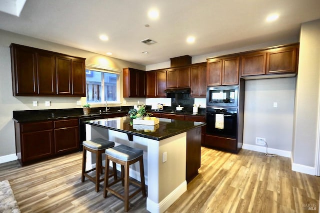 kitchen with visible vents, dishwashing machine, stainless steel microwave, black oven, and light wood-type flooring