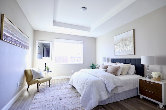 bedroom with baseboards, a tray ceiling, and dark wood-type flooring