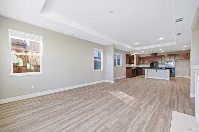 unfurnished living room featuring a tray ceiling, visible vents, baseboards, recessed lighting, and light wood-style floors