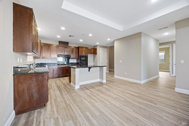 kitchen featuring light wood finished floors, a breakfast bar, visible vents, a sink, and black microwave
