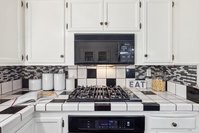 kitchen featuring tile countertops, white cabinets, black microwave, and oven