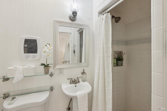 bathroom with toilet, tiled shower, heating unit, and a sink