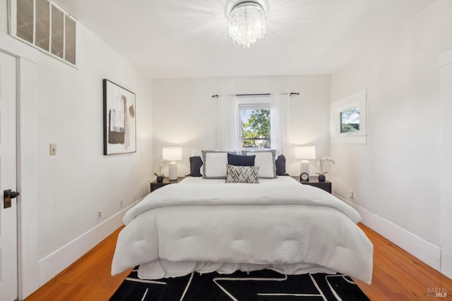 bedroom with a chandelier, visible vents, light wood finished floors, and baseboards