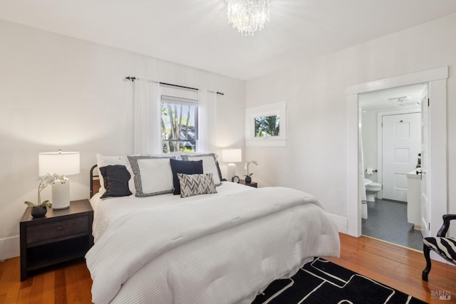 bedroom with a chandelier, wood finished floors, and ensuite bath