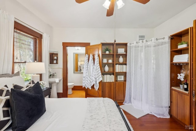 bedroom with connected bathroom, wood finished floors, visible vents, and a sink
