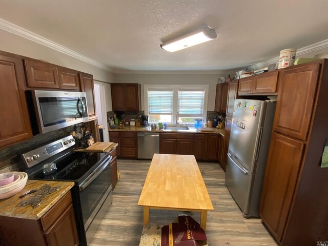 kitchen with light wood-style floors, crown molding, stainless steel appliances, and a sink