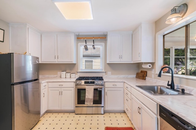 kitchen featuring light stone counters, a sink, light floors, white cabinetry, and appliances with stainless steel finishes