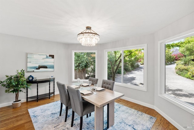 dining room featuring wood finished floors, a wealth of natural light, baseboards, and an inviting chandelier