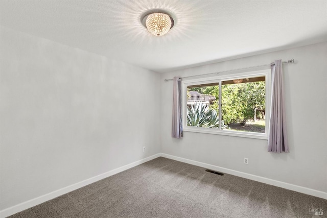 spare room with carpet floors, an inviting chandelier, visible vents, and baseboards