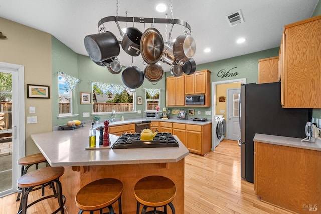 kitchen with stainless steel appliances, a kitchen breakfast bar, a peninsula, washer and clothes dryer, and visible vents