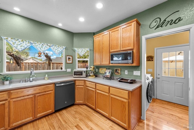 kitchen featuring dishwashing machine, a sink, stainless steel microwave, light wood-type flooring, and washing machine and clothes dryer