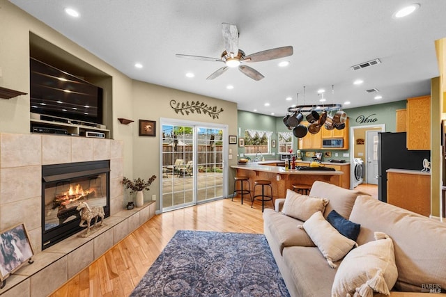 living area featuring light wood-style flooring, ceiling fan, washer / dryer, a fireplace, and visible vents