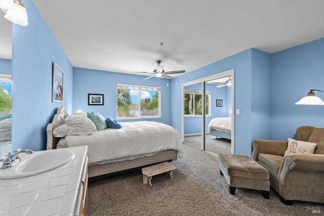 carpeted bedroom with a closet, a ceiling fan, and a sink