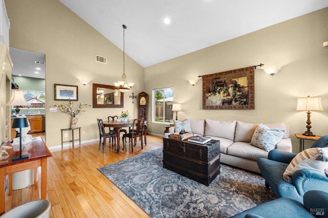living area featuring high vaulted ceiling, light wood finished floors, baseboards, a notable chandelier, and visible vents