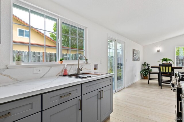 240 Rinaldo Dr, Vallejo, CA 94589 - kitchen with vaulted ceiling, gray cabinets, a sink, light wood-type flooring, and light stone countertops