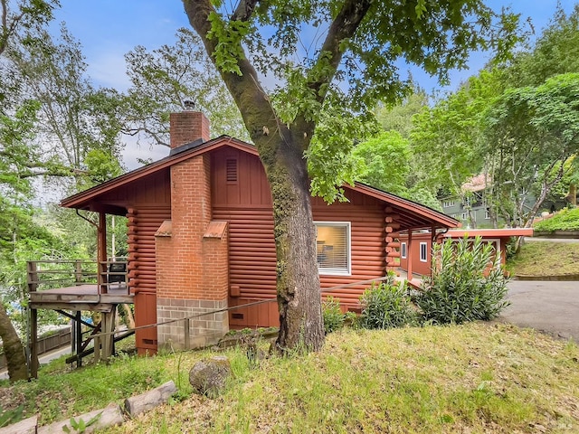 view of property exterior with a chimney, a wooden deck, and log siding