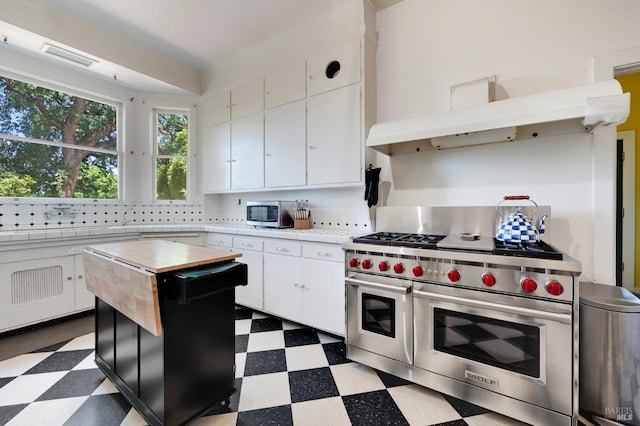 kitchen with white cabinets, double oven range, decorative backsplash, light floors, and under cabinet range hood