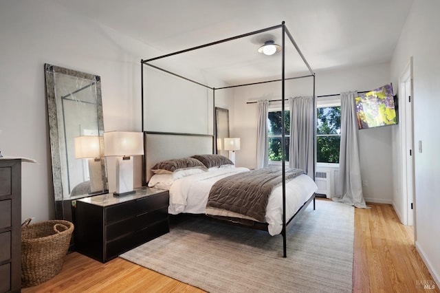 bedroom featuring baseboards, light wood-style floors, and radiator