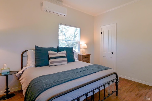 bedroom featuring a wall mounted AC, wood finished floors, baseboards, and ornamental molding