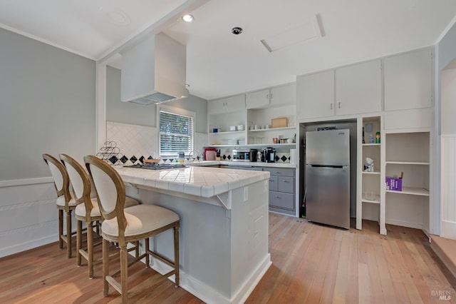 kitchen with open shelves, extractor fan, tile countertops, a peninsula, and appliances with stainless steel finishes