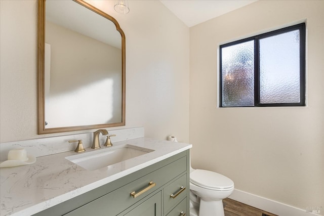 half bathroom with toilet, vanity, wood finished floors, and baseboards
