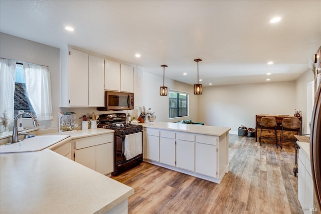 kitchen with a peninsula, a sink, stainless steel microwave, black gas range, and light wood-style floors