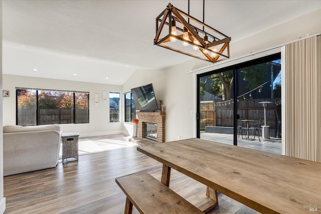 unfurnished dining area with lofted ceiling, a brick fireplace, wood finished floors, and recessed lighting