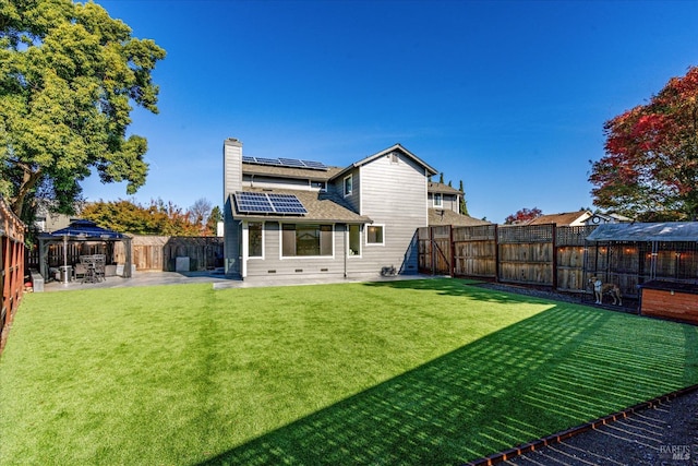 rear view of property featuring a fenced backyard, a yard, solar panels, a patio area, and a gazebo