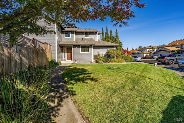 traditional-style house featuring a residential view, a shingled roof, a front lawn, and fence