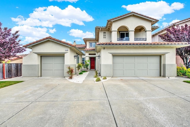mediterranean / spanish-style house with stucco siding, fence, concrete driveway, and a tiled roof