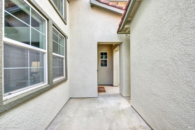 view of exterior entry with a patio, a tiled roof, and stucco siding