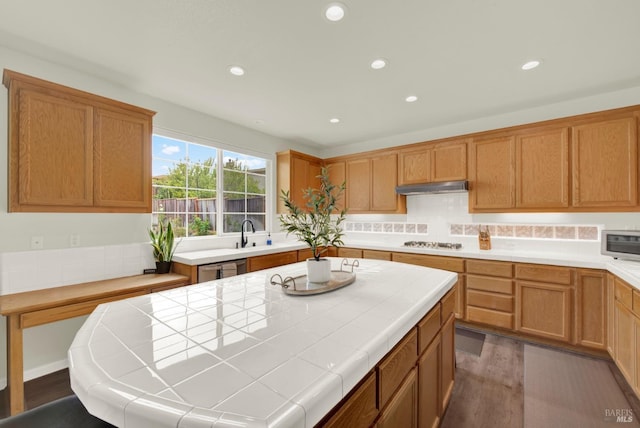 kitchen featuring tile counters, under cabinet range hood, wood finished floors, gas cooktop, and a kitchen island