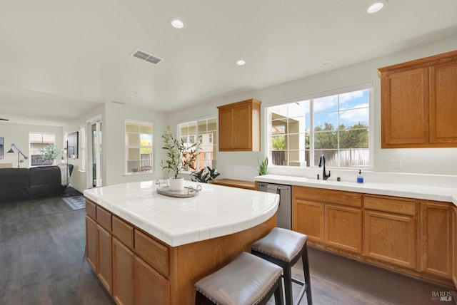 kitchen featuring dark wood finished floors, dishwasher, a sink, a wealth of natural light, and a center island