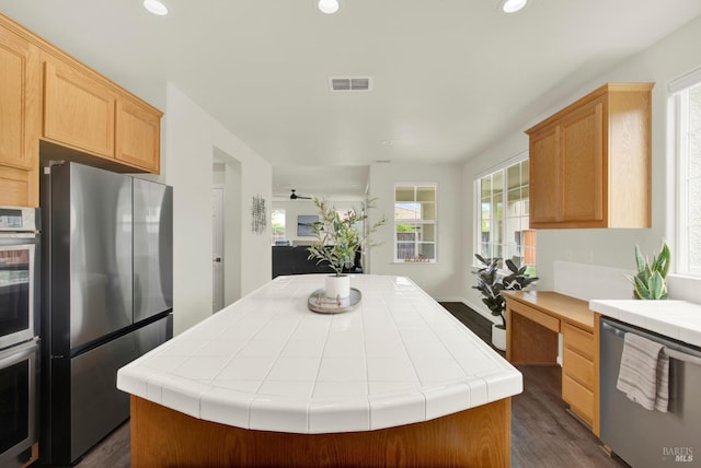 kitchen featuring a center island, appliances with stainless steel finishes, tile countertops, and dark wood-style floors