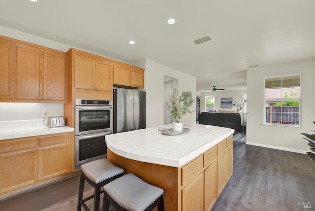 kitchen featuring a center island, tile counters, visible vents, appliances with stainless steel finishes, and dark wood-style floors