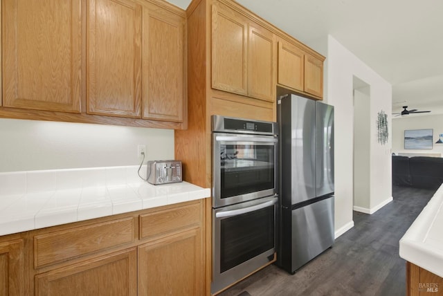 kitchen with stainless steel appliances, dark wood-style flooring, baseboards, a ceiling fan, and tile countertops