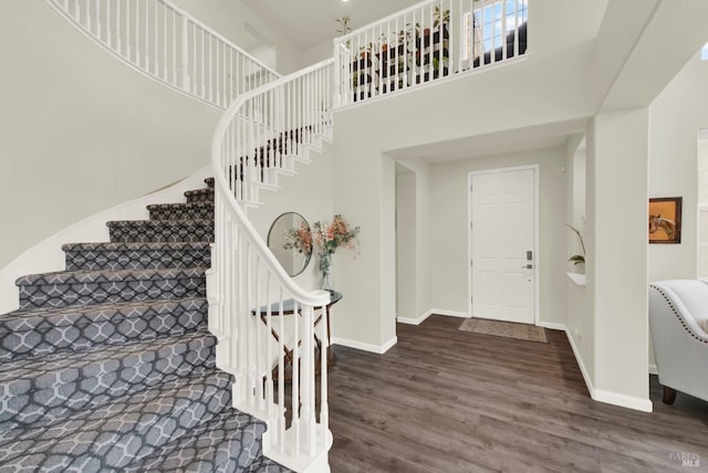 entryway featuring baseboards, wood finished floors, and a towering ceiling