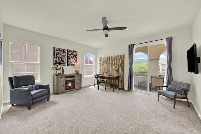 living area featuring a warm lit fireplace, carpet, a ceiling fan, and baseboards