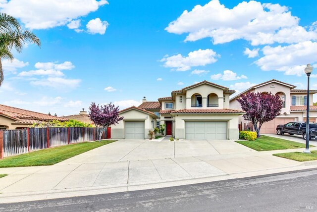 mediterranean / spanish-style house with a tiled roof, concrete driveway, fence, a garage, and stucco siding