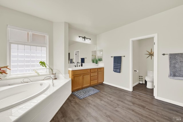 full bath featuring wood finished floors, a bath, vanity, baseboards, and toilet