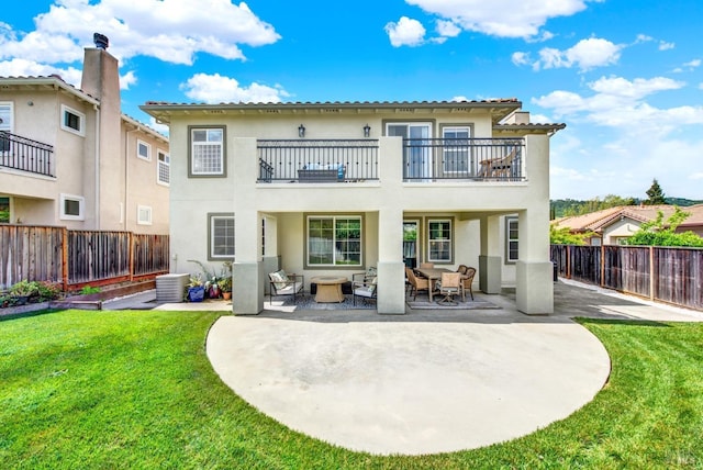rear view of property featuring stucco siding, a balcony, a fenced backyard, and a lawn